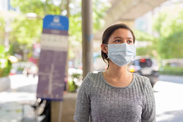 Portrait of young Filipino woman with mask for protection from corona virus outbreak at the bus stop in the city outdoors