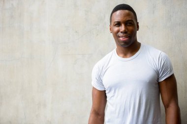 Portrait of young handsome muscular African man against concrete wall outdoors