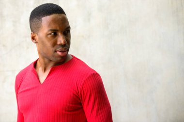 Portrait of young handsome muscular African man against concrete wall outdoors