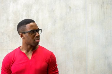 Portrait of young handsome muscular African man with eyeglasses against concrete wall outdoors