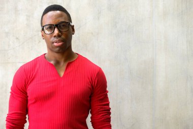 Portrait of young handsome muscular African man with eyeglasses against concrete wall outdoors