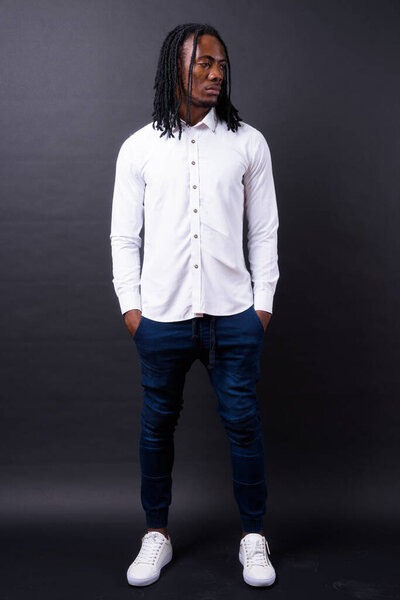 Studio shot of young handsome African businessman with dreadlocks against black background