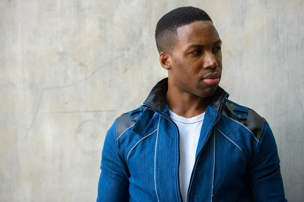 Portrait of young handsome muscular African man wearing blue jacket against concrete wall outdoors