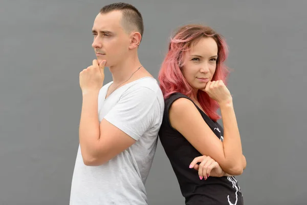 Portrait of handsome man and beautiful woman with pink hair as couple together and in love against gray wall outdoors