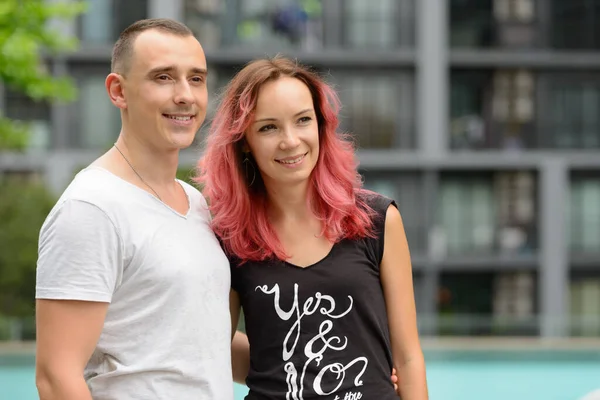 Portrait of handsome man and beautiful woman with pink hair as couple together in the swimming pool area outdoors