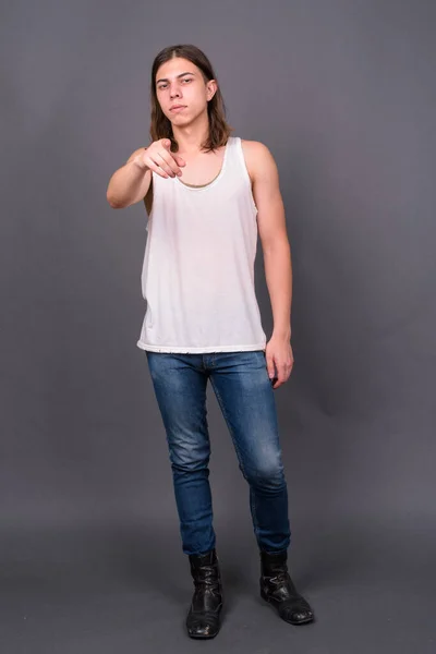 Studio shot of young handsome androgynous man with long hair against gray background