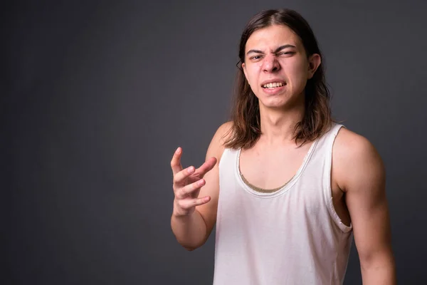 Studio shot of young handsome androgynous man with long hair against gray background