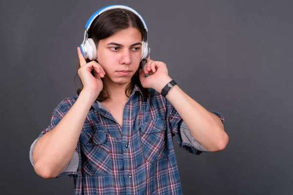 Studio shot of young handsome androgynous hipster man with long hair against gray background