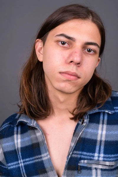 Studio shot of young handsome androgynous hipster man with long hair against gray background