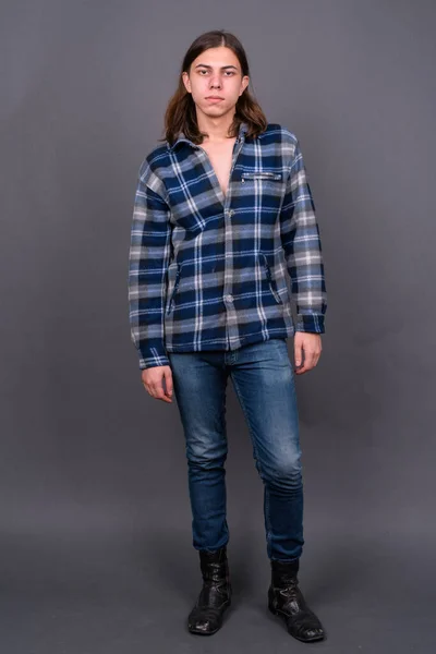 Studio shot of young handsome androgynous hipster man with long hair against gray background