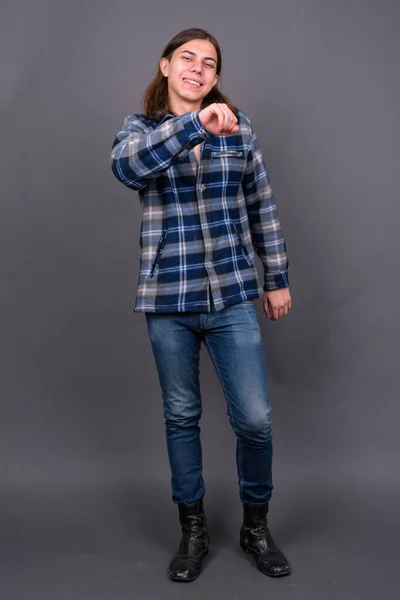 Studio shot of young handsome androgynous hipster man with long hair against gray background