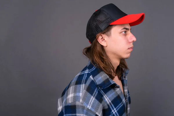 Studio shot of young handsome androgynous hipster man with long hair against gray background