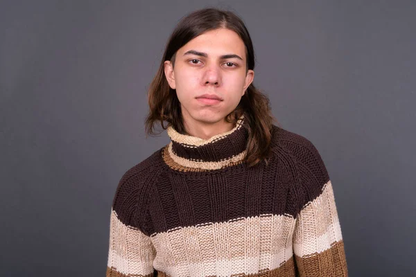 Studio shot of young handsome androgynous man with long hair ready for winter against gray background