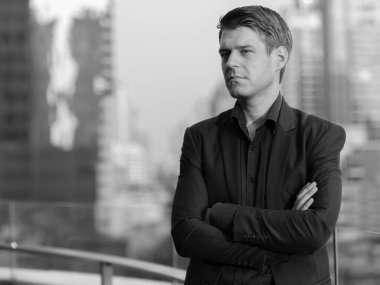 Portrait of young handsome businessman in suit against view of the city in black and white