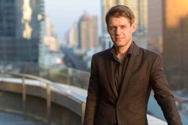 Portrait of young handsome businessman in suit against view of the city