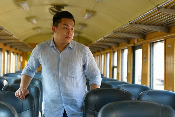 Portrait of young handsome overweight Filipino tourist man riding inside the train