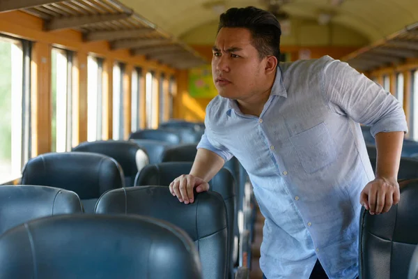 Portrait of young handsome overweight Filipino tourist man riding inside the train