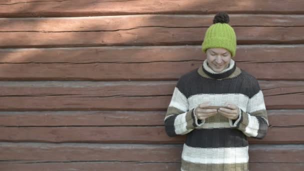 Jovem feliz usando telefone contra parede de madeira no outono — Vídeo de Stock