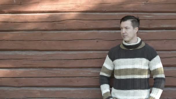 Щасливий молодий чоловік посміхається на дерев'яну стіну восени — стокове відео
