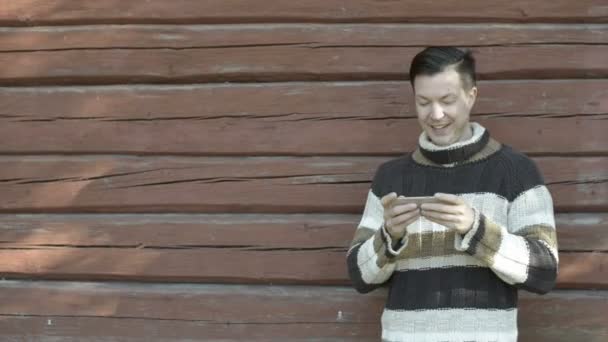 Jovem feliz usando telefone contra parede de madeira no outono — Vídeo de Stock