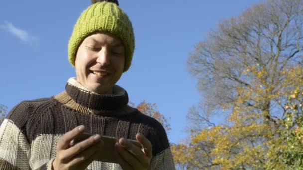 Обличчя щасливого молодого чоловіка, який використовує телефон у парку восени — стокове відео