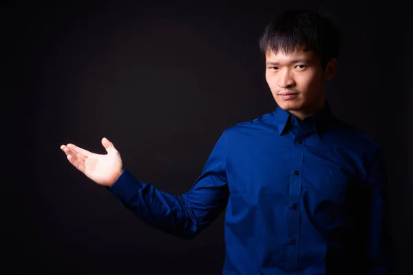 Studio shot of young Chinese businessman wearing blue shirt against black background