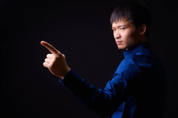 Studio shot of young Chinese businessman wearing blue shirt against black background