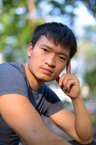 Portrait de jeune homme asiatique assis au parc en plein air — Photo