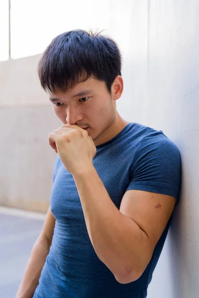 Портрет молодого азіата, який думає проти стіни на відкритому повітрі. — стокове фото