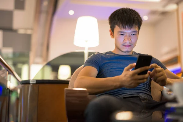 Портрет молодого азіата, який користується телефоном і сидить у торговому центрі. — стокове фото