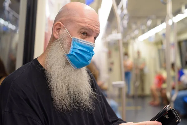 Arca érett kopasz szakállas férfi maszk gondolkodás használata közben telefon a vonaton — Stock Fotó