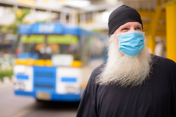Volwassen bebaarde hipster man met masker denken terwijl het wachten bij de bushalte — Stockfoto