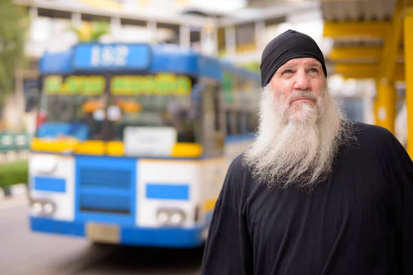 Зрелый красивый бородатый хипстер думает и ждет на автобусной остановке — стоковое фото