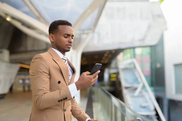 Ung stilig afrikansk affärsman använder telefon på gångbro i staden — Stockfoto