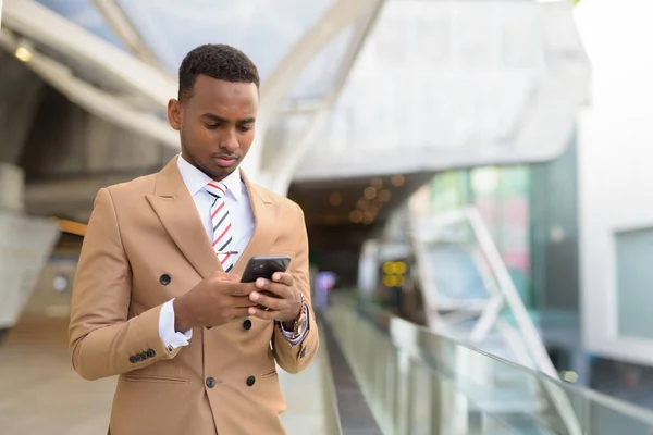 Young handsome African businessman using phone at the footbridge — Stock Photo, Image