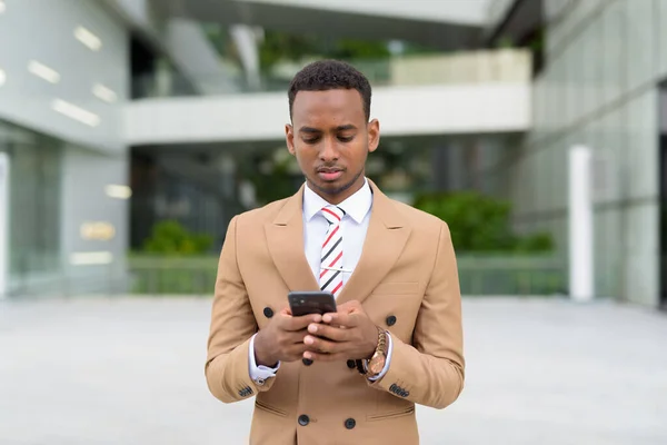 Young handsome African businessman using phone in the city outdoors — Stock Photo, Image