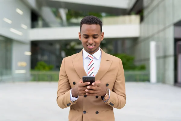 Happy young handsome African businessman using phone in the city — Stock Photo, Image