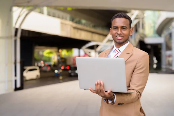 Jovem empresário africano feliz usando laptop na cidade ao ar livre — Fotografia de Stock