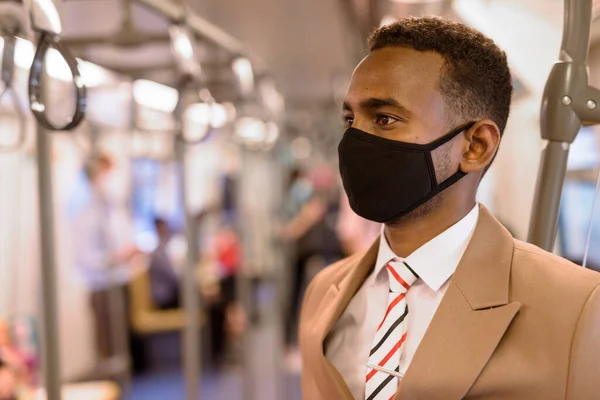 Arca fiatal afrikai üzletember maszkot visel, és áll a távolság a vonaton belül — Stock Fotó