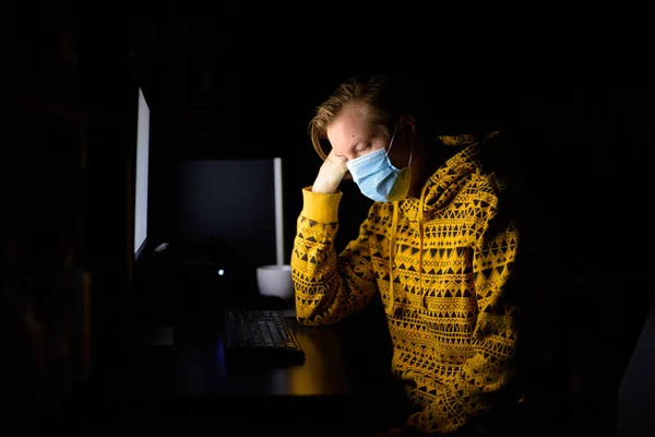 Portrait of young man with mask for protection from corona virus outbreak working from home during quarantine late at night