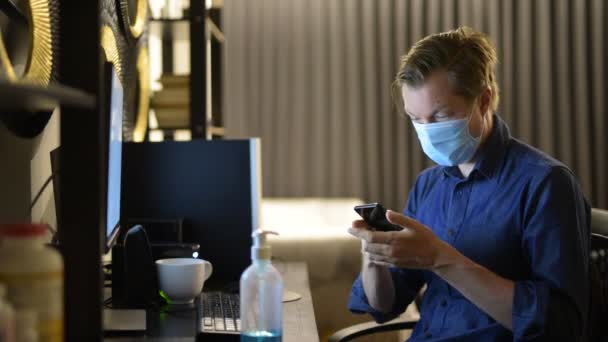 Giovane uomo d'affari con maschera video chiamata con telefono mentre si lavora da casa a tarda notte — Video Stock