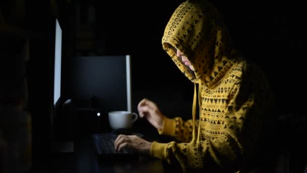 Giovane uomo con cappuccio come hacker utilizzando il telefono e il computer al buio — Video Stock