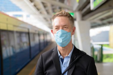 Portrait of mature businessman with mask for protection from corona virus outbreak at the sky train station