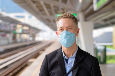 Portrait of mature businessman with mask for protection from corona virus outbreak at the sky train station