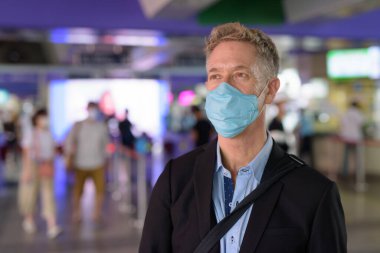Portrait of mature businessman with mask for protection from corona virus outbreak at the sky train station