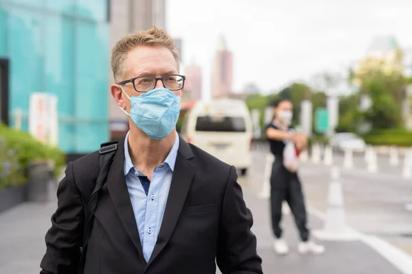 Portrait of mature businessman with mask for protection from corona virus outbreak in the city streets outdoors