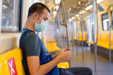 Portrait of young Asian man wearing mask for protection from corona virus outbreak social distancing inside the train