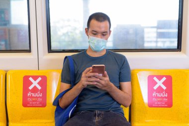 Portrait of young Asian man wearing mask for protection from corona virus outbreak social distancing inside the train