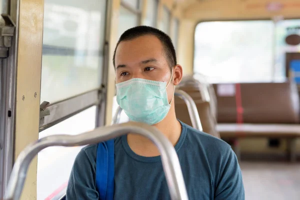 Portrait of young Asian man with mask for protection from corona virus outbreak riding the bus in the city outdoors