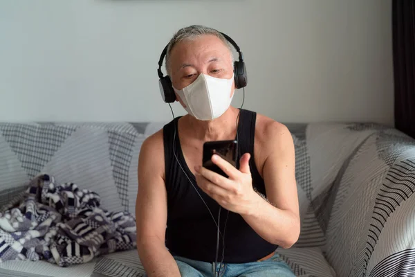 Portrait of mature Japanese man with mask for protection from corona virus outbreak at home under quarantine